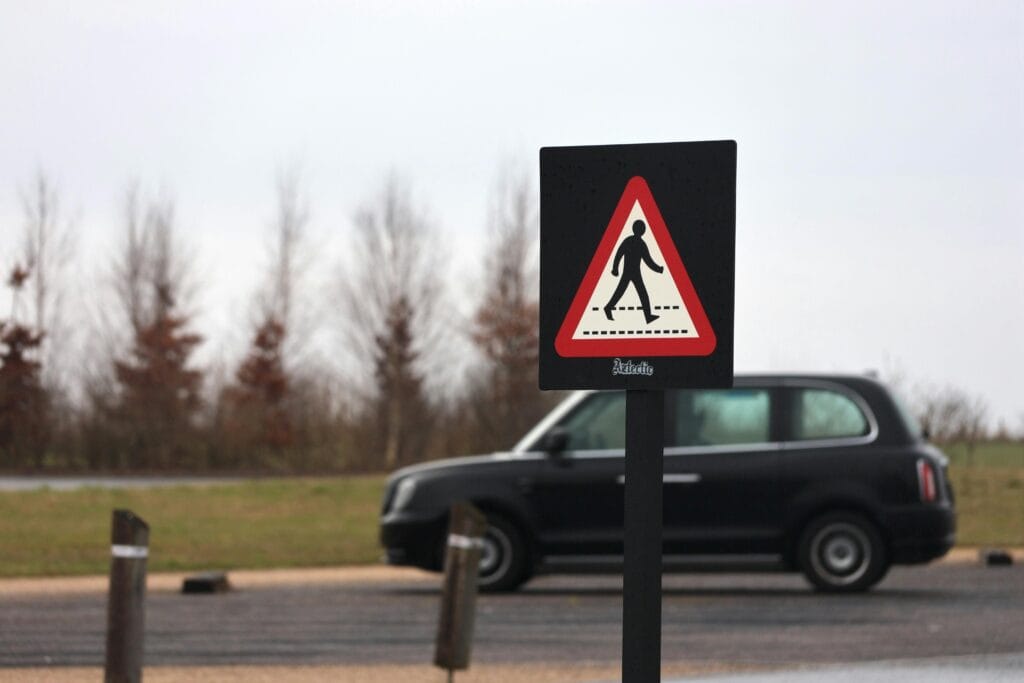 pexels-photo-30834703-30834703-1 A pedestrian crossing sign with a black taxi in the background on a quiet road.